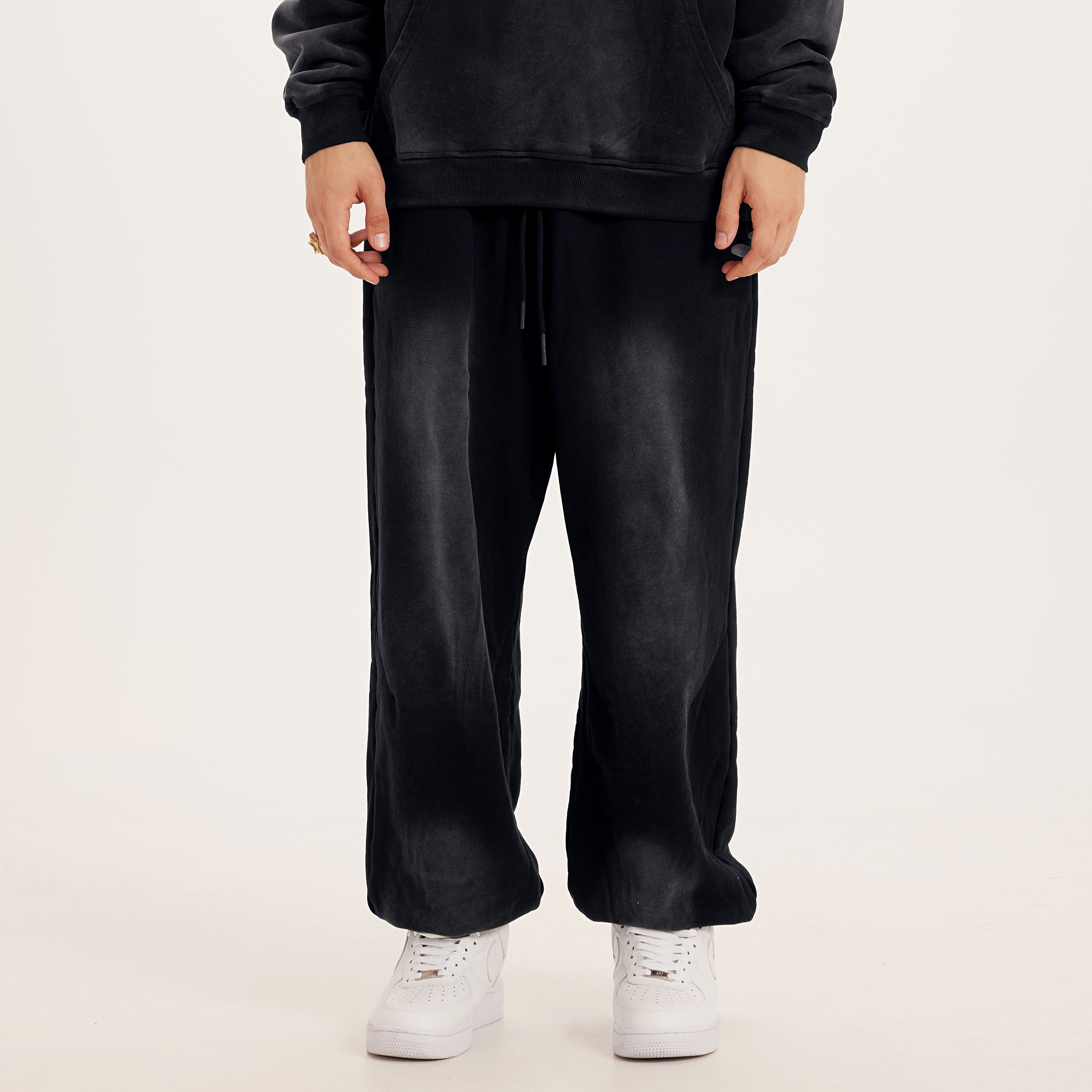 Front of luxury streetwear black oversized pants in baggy sweatpants style, washed black color streetwear pants, model with white streetwear shoes
