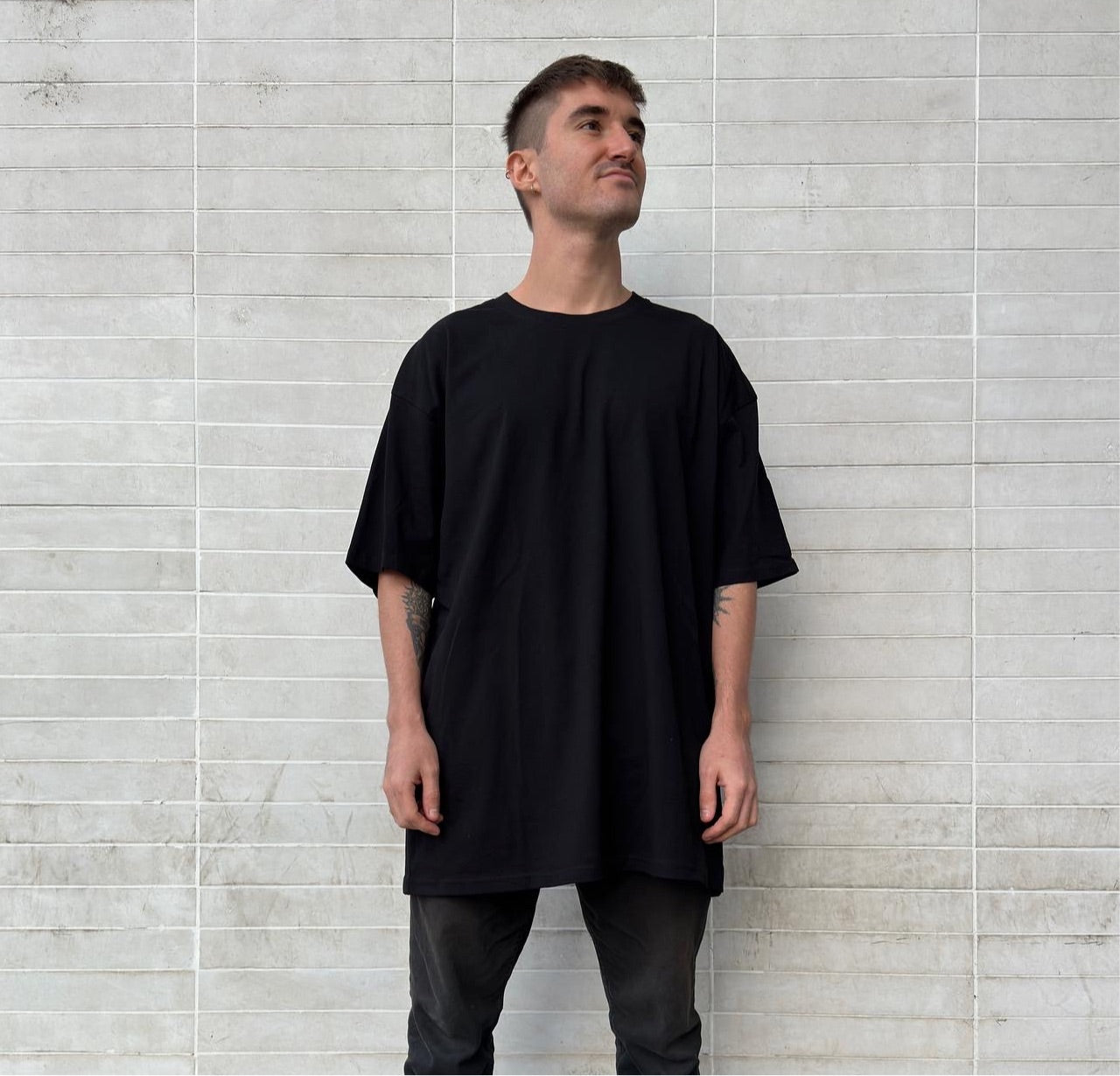 Luxury streetwear model wearing black t-shirt oversized drop shoulder tee against urban wall