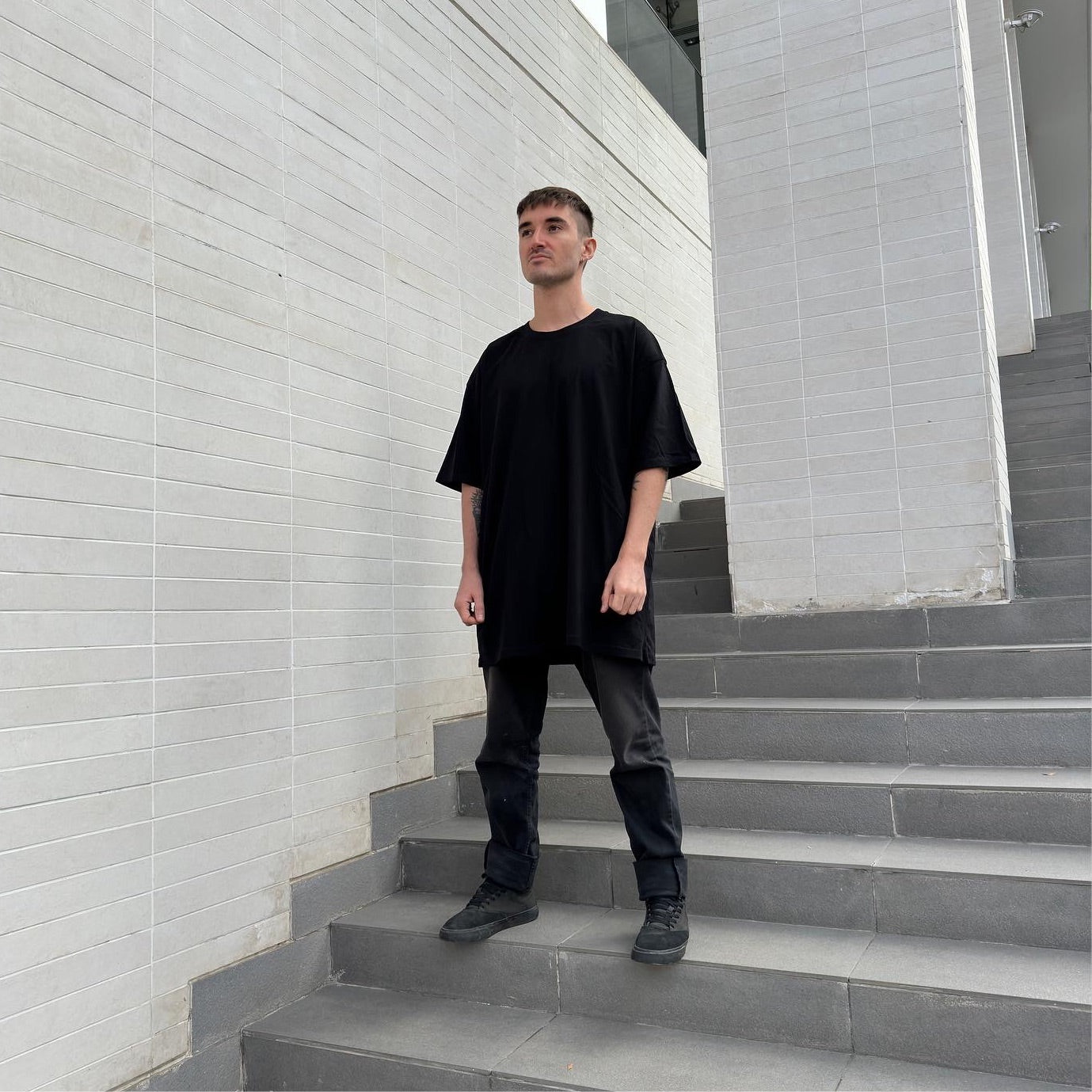 Streetwear model wearing full black with black oversized t-shirt standing on an urban staircase