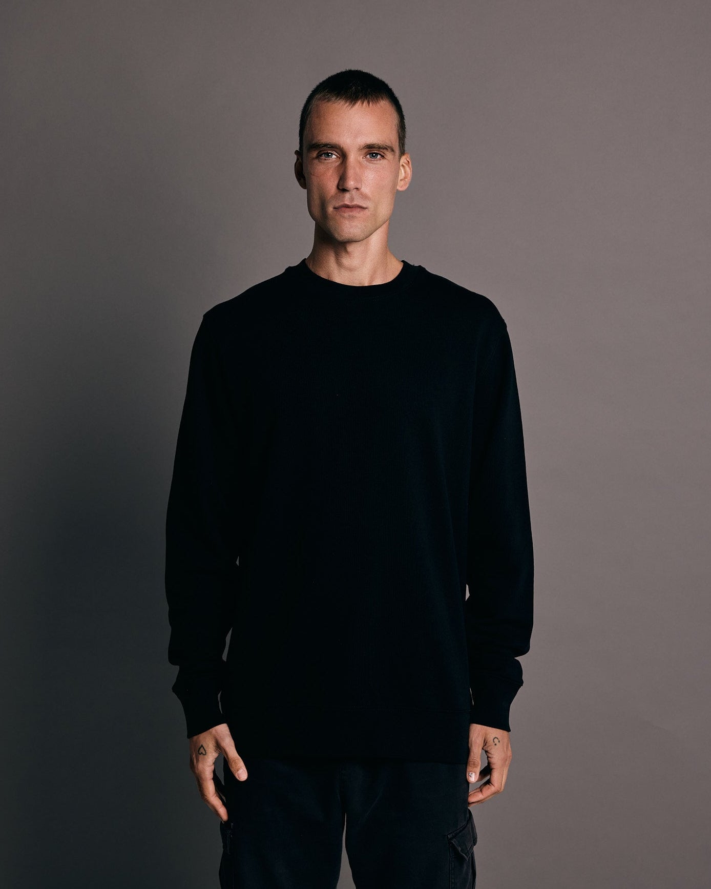 Man wearing a black sweatshirt and pants against a gray background