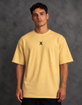 Model wearing a golden yellow t-shirt with a small black X centered on the chest, a crew neck and short sleeves.
