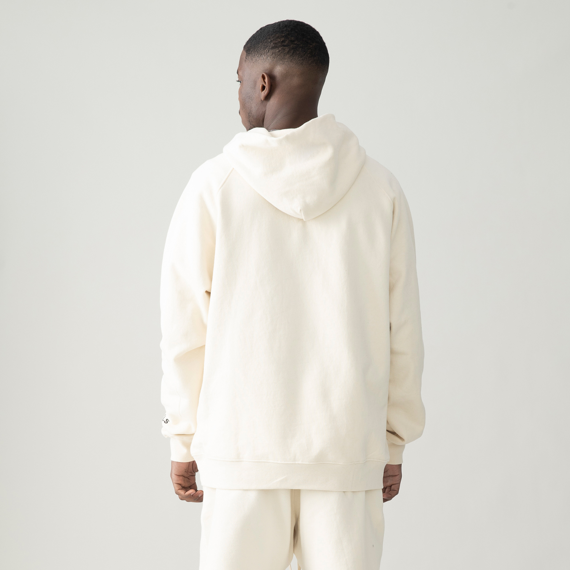 back view of model wearing off white hoodie and off white pants, his face turned to the side