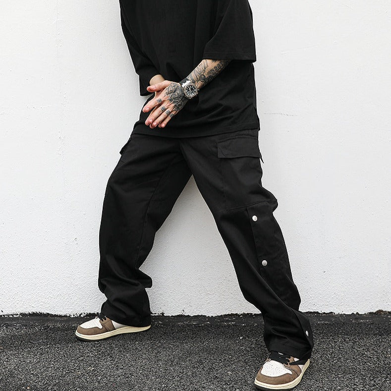 model wearing luxury streetwear black outfit with black cargo pants, standing with legs, against white wall apart, hands together