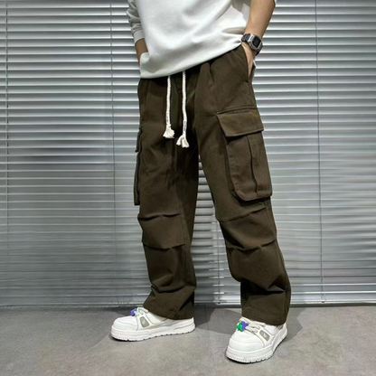 brown cargo pants for men, model's hand inside side pockets, front view, white drawstrings, utility pockets