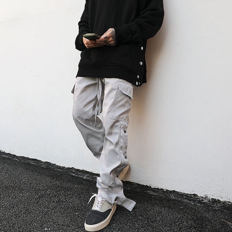 model leaning against the wall on phone wearing grey cargo pants with snap ankle, luxury streetwear aesthetic