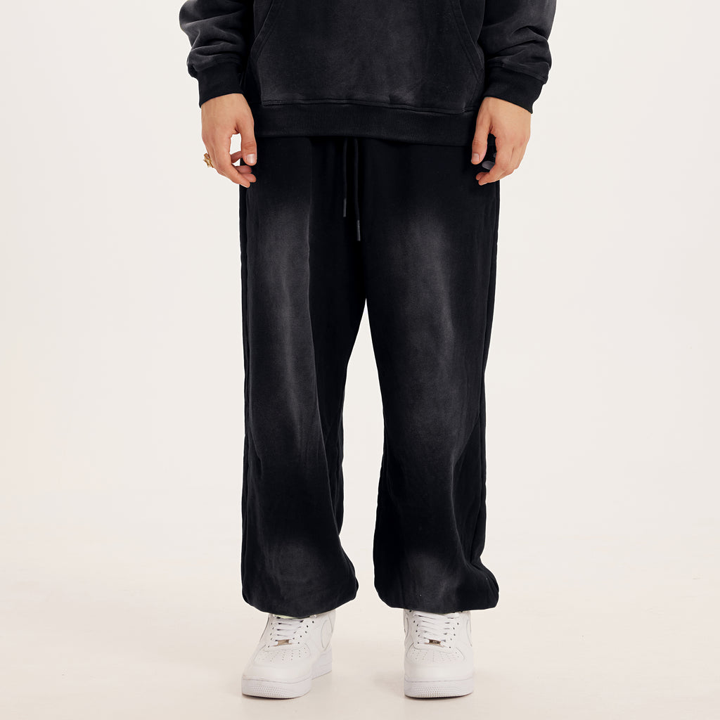Front of luxury streetwear black oversized pants in baggy sweatpants style, washed black color streetwear pants, model with white streetwear shoes 