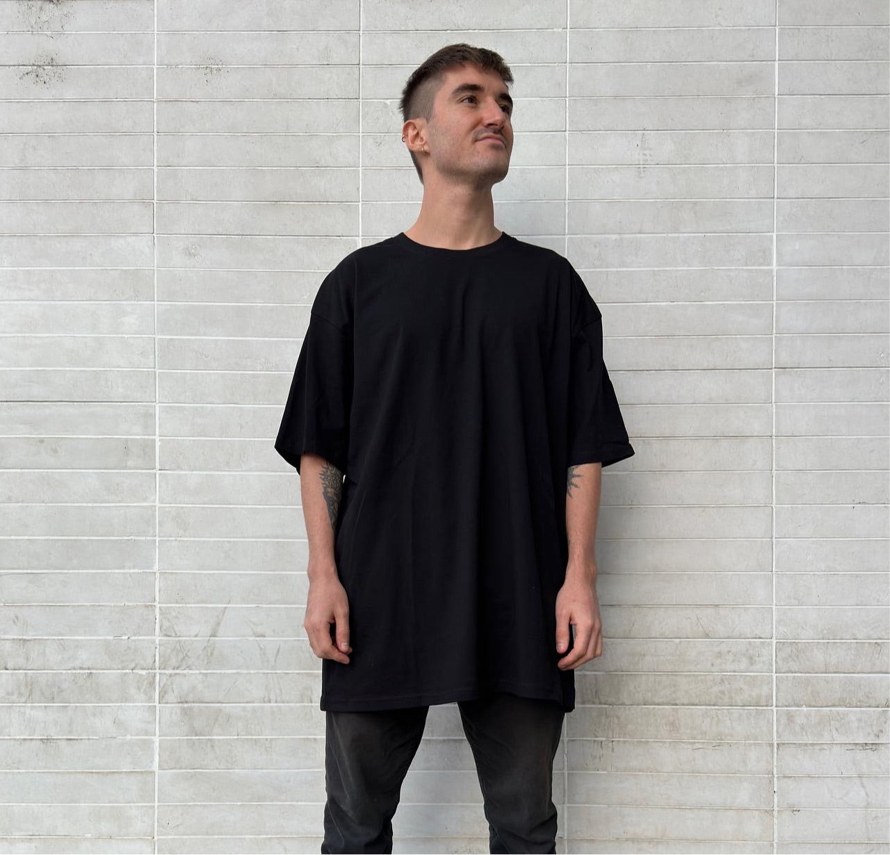 Luxury streetwear model wearing black t-shirt oversized drop shoulder tee against urban wall 
