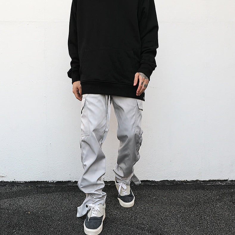 model against white wall wearing luxury streetwear black hoodie and light grey cargo pants with ankle snap