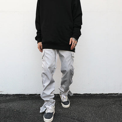 model against white wall wearing luxury streetwear black hoodie and light grey cargo pants with ankle snap