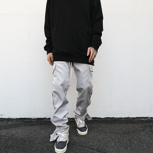 model against white wall wearing luxury streetwear black hoodie and light grey cargo pants with ankle snap