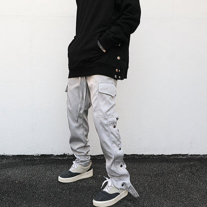 model with hands in hoodie pocket showing luxury streetwear light grey cargo pants with side leg buttons and ankle snap in modern look