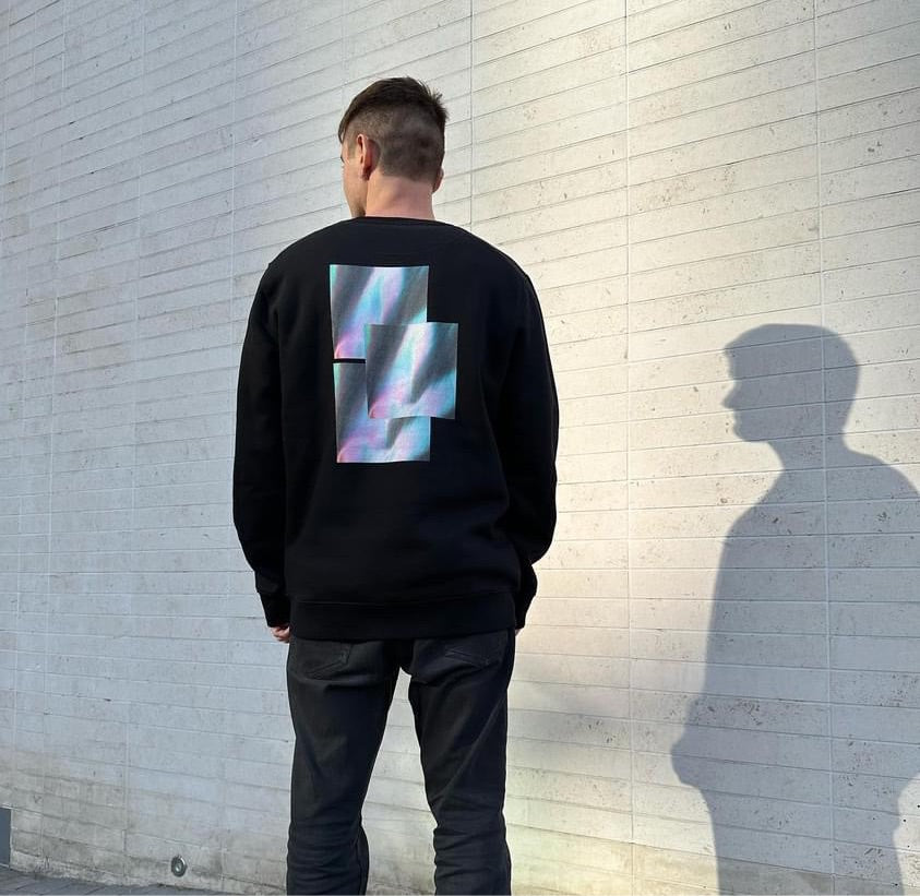 Male model wearing black crewneck sweatshirt ‘reflect’ graphic luxury streetwear against grey wall with shadow casting