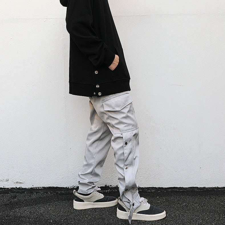 side of model wearing light grey cargo pants with ankle snap and black hoodie, hands in pocket