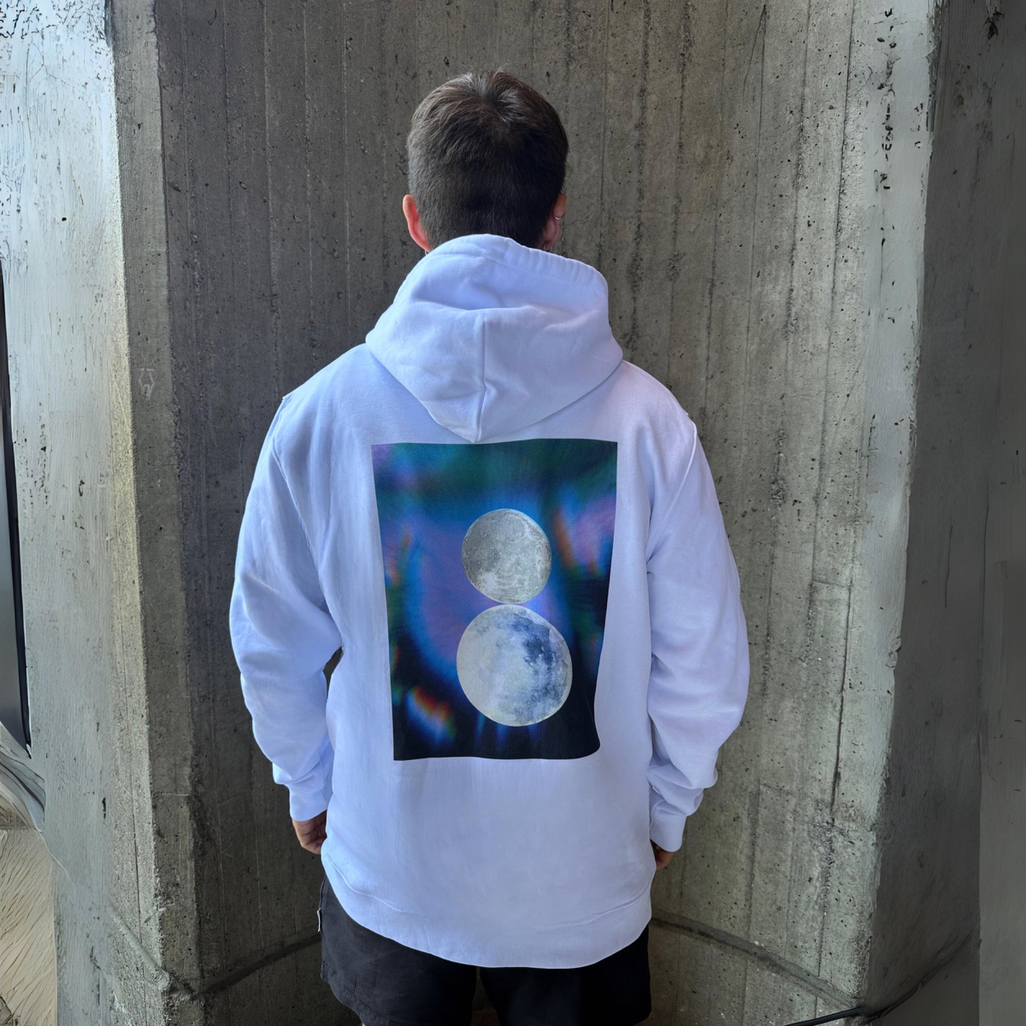 back view of male model wearing white graphic hoodie with square design of 2 moons and faded colors, 'Materialise' white hoodie by AETERIUS