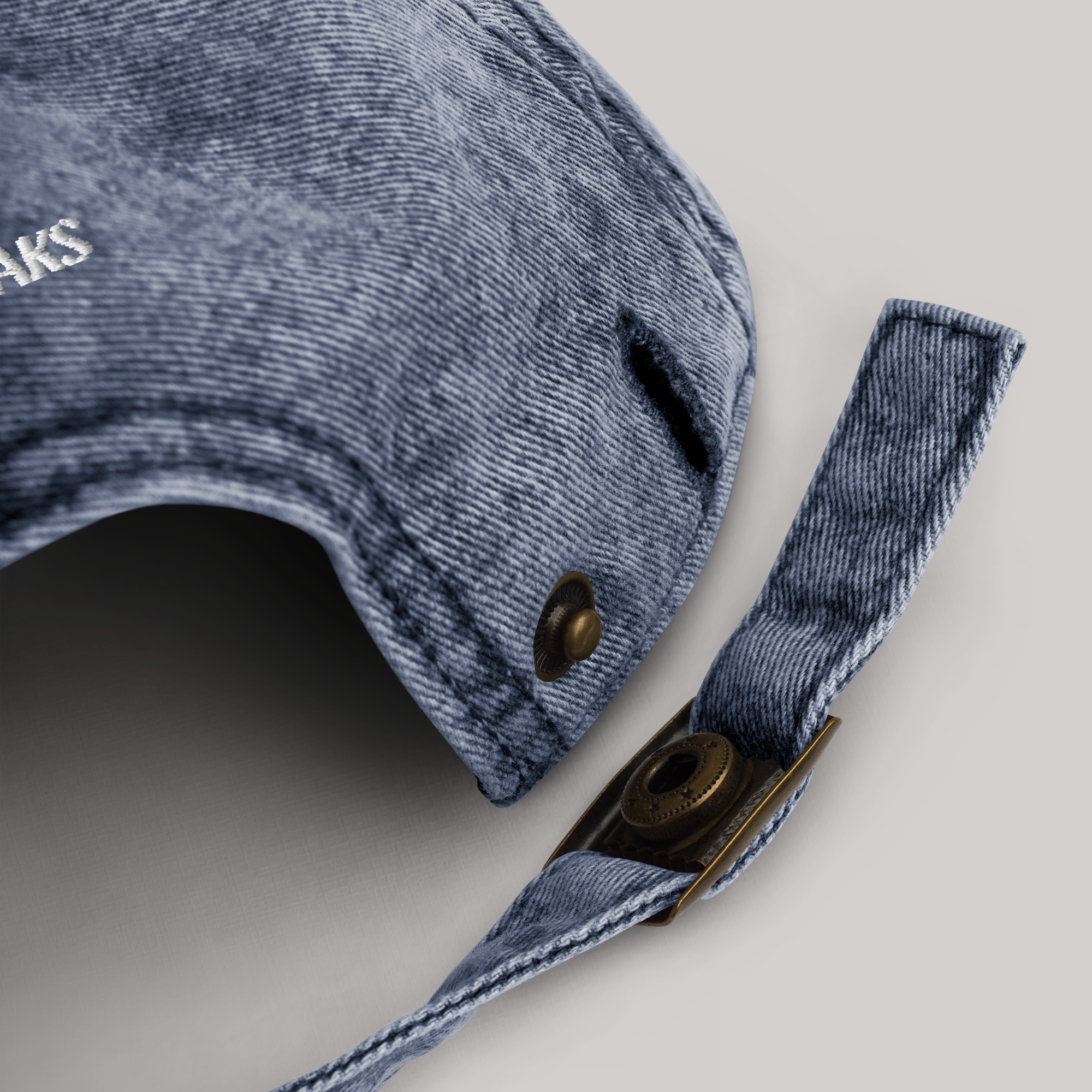 Adjustable buckle of cap, back side. Button off/open. Denim washed out color