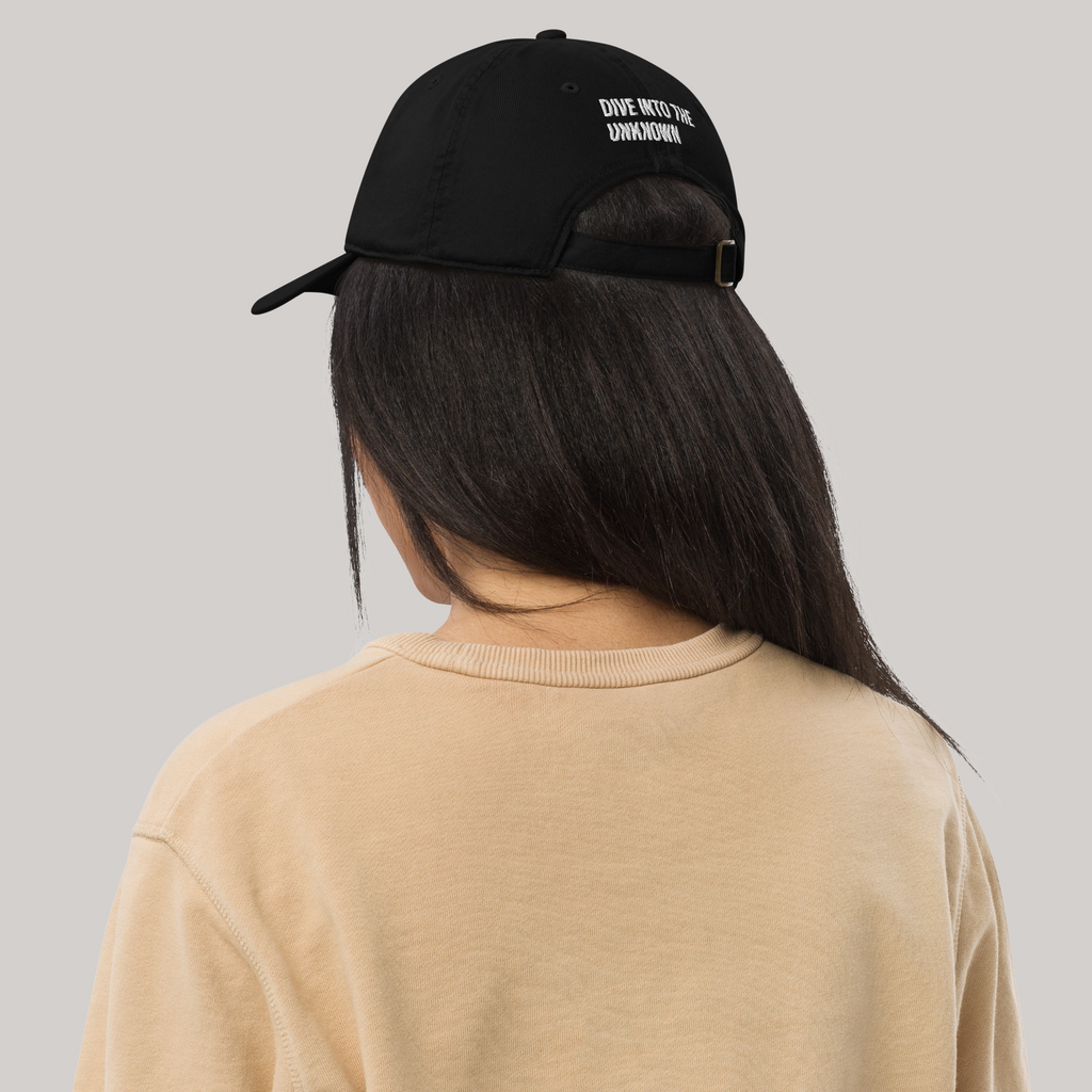 Female model wearing organic baseball cap black 'dive into the unknown' embroidery long black hair beige sweater back side
