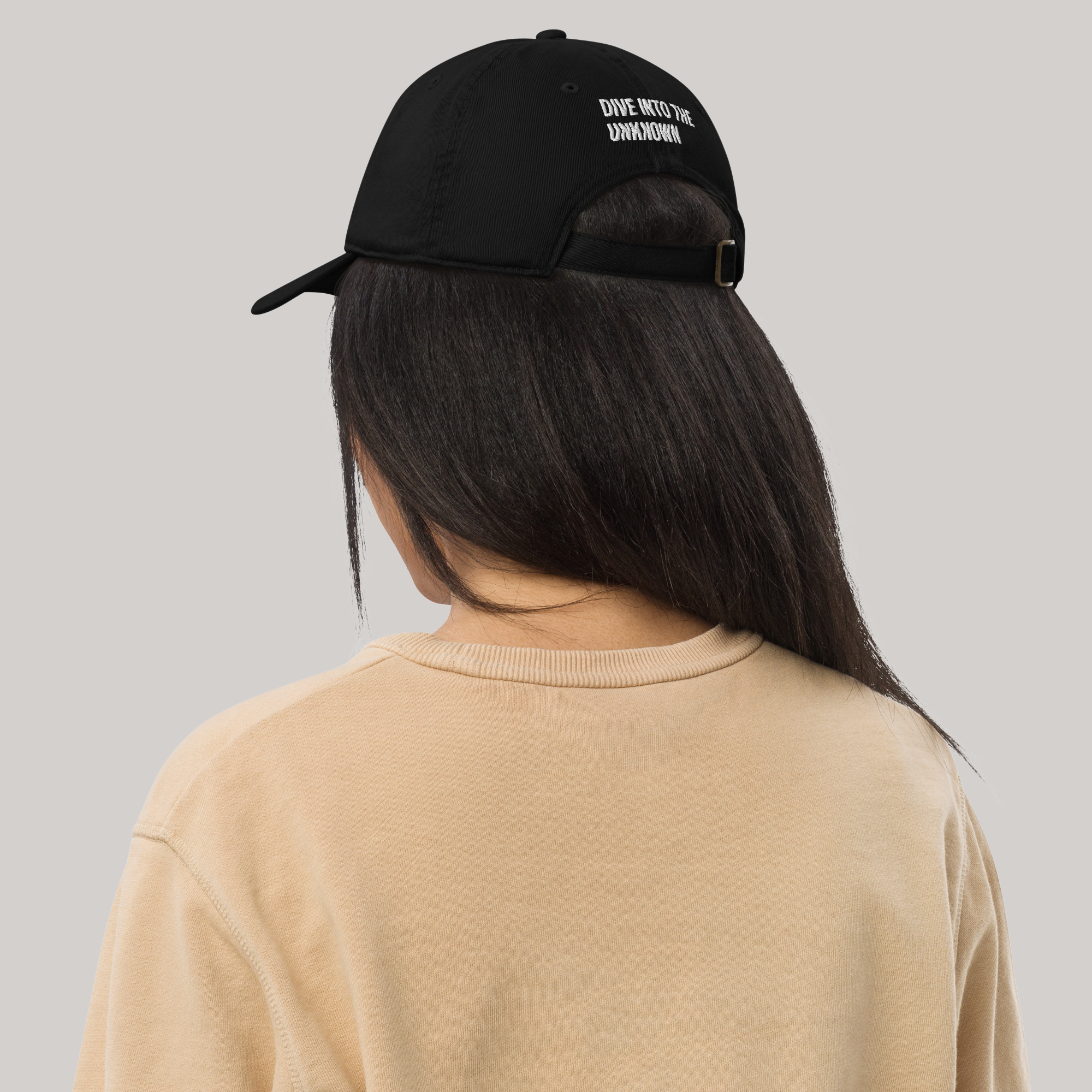 Female model wearing organic baseball cap black 'dive into the unknown' embroidery long black hair beige sweater back side